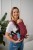 Modelka nosi dziecko w ergonomicznego nosidle KAVKA Multi‑Age burgundy braid cotton - burgundowe nosidło z białym wzorem warkocza