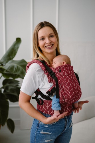 Modelka nosi dziecko w ergonomicznego nosidle KAVKA Multi‑Age burgundy braid cotton - burgundowe nosidło z białym wzorem warkocza
