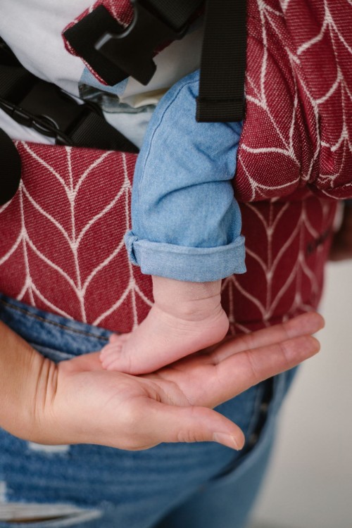 Modelka nosi dziecko w ergonomicznego nosidle KAVKA Multi‑Age burgundy braid cotton - burgundowe nosidło z białym wzorem warkocza