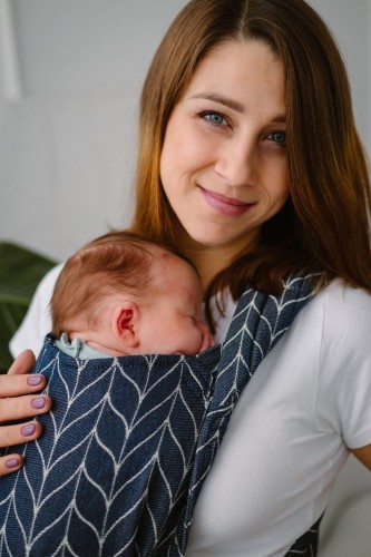 Modelka nosi dziecko w wiązanym ergonomicznym nosidle KAVKA handy ink braid cotton - granatowe nosidło z białym wzorem warkocza (ink braid cotton with white braid pattern)