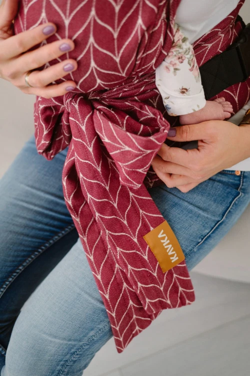 Modelka nosi dziecko w ergonomicznego nosidle KAVKA handy burgundy braid cotton - burgundowe nosidło z białym wzorem warkocza (burgundy carrier with a white braid pattern)