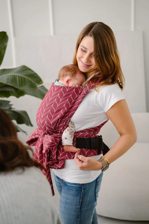 Modelka nosi dziecko w ergonomicznego nosidle KAVKA handy burgundy braid cotton - burgundowe nosidło z białym wzorem warkocza (burgundy carrier with a white braid pattern)