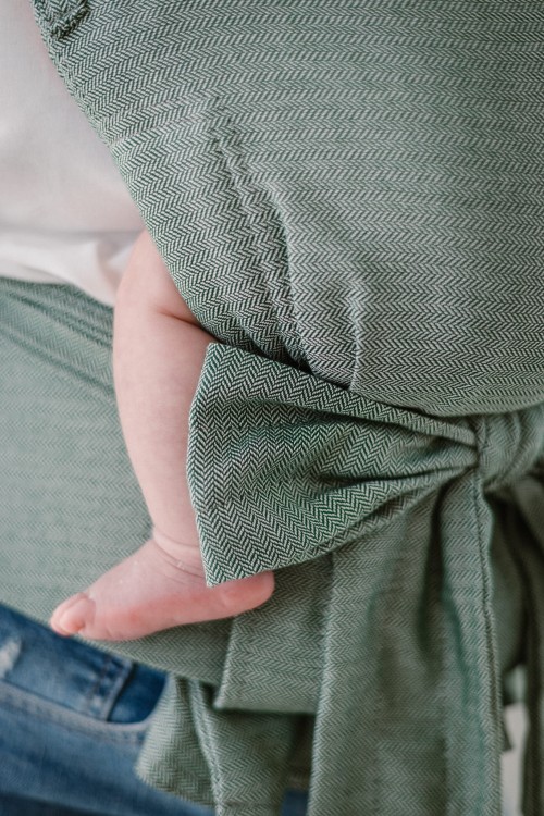 Modelka nosi dziecko w ergonomicznym nosidle KAVKA handy fern twill -  zielone nosidło z delikatnym wzorem w jodełkę. (a green carrier with a delicate herringbone - twill pattern)
