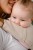 Modelka nosi dziecko w ergonomicznym nosidle KAVKA handy vanilla twill -  beżowe nosidło z białym  wzorem w drobną jodełkę  (a beige baby carrier with white twill  pattern)
